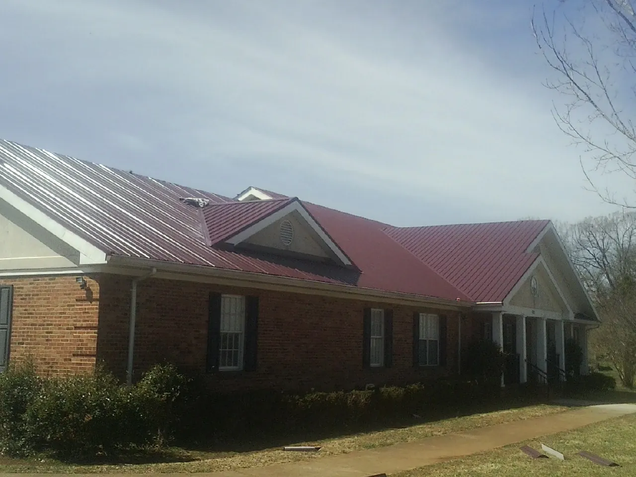 Red metal roof with gabled entries on a long brick building, from a Hail Damage Roof Repair job in Wallpack Center