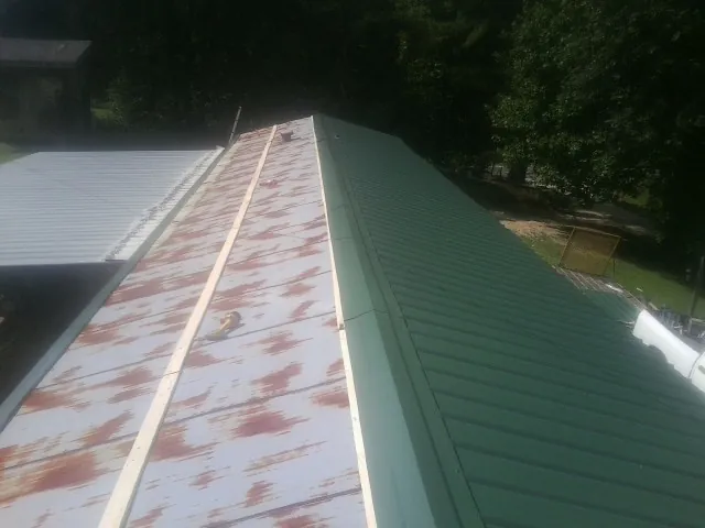 Old rusted panels beside newly installed green metal roofing — Wind Damage Roof Repair by Roofing Brothers in Wallpack Center