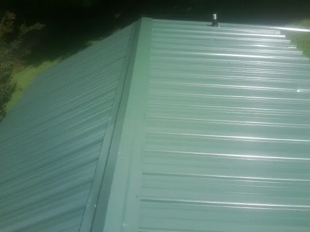 New green metal panels meeting at the ridge of a roof — Flat Roof Repair work by our crew in Wallpack Center