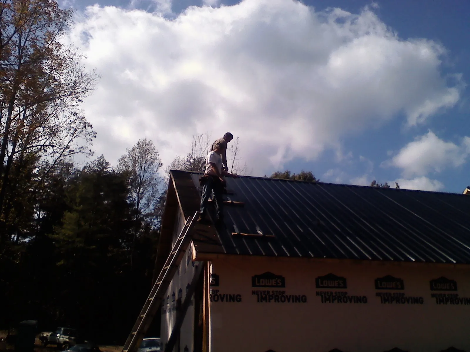 Roofer fastening dark metal panels high against a cloudy sky, from a Roof Inspection job in Wallpack Center