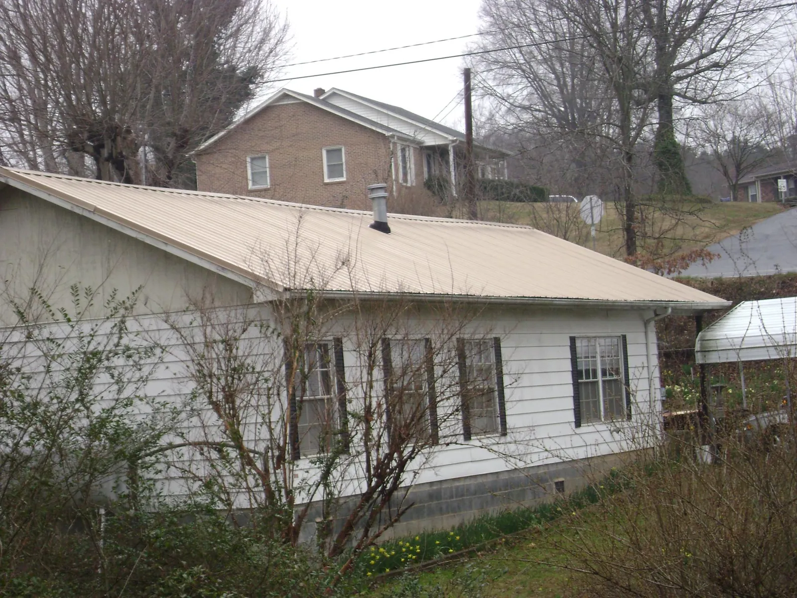 Tan metal roof on a white sided house set into a hillside — Commercial Roofing by Roofing Brothers in Wallpack Center